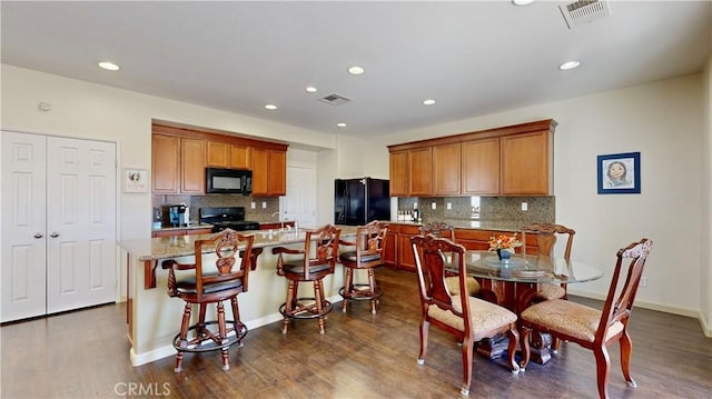 kitchen with a breakfast bar, backsplash, dark wood-type flooring, black appliances, and a kitchen island