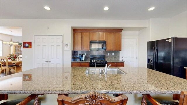 kitchen featuring black appliances, a center island with sink, light stone countertops, and sink