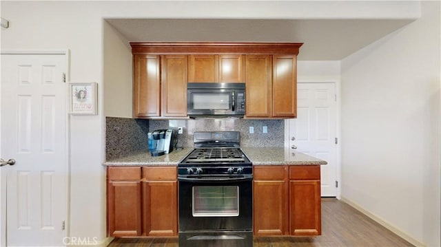 kitchen with backsplash, dark hardwood / wood-style floors, light stone counters, and black appliances