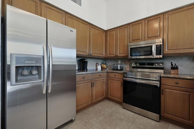 kitchen featuring dark stone counters, light tile patterned floors, appliances with stainless steel finishes, and tasteful backsplash