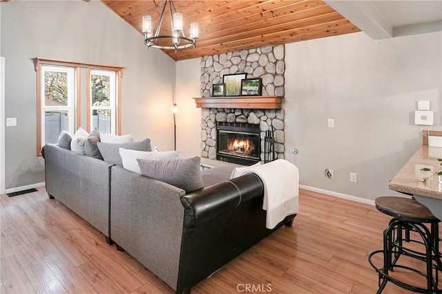 living room with wood ceiling, vaulted ceiling, an inviting chandelier, light hardwood / wood-style flooring, and a stone fireplace