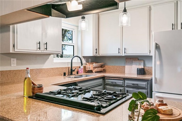 kitchen with pendant lighting, stainless steel gas stovetop, sink, white fridge, and white cabinetry