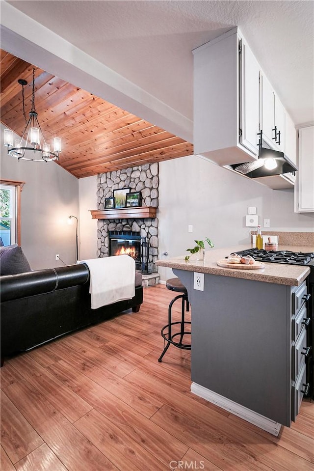 kitchen featuring white cabinetry, light hardwood / wood-style flooring, pendant lighting, a kitchen bar, and a fireplace