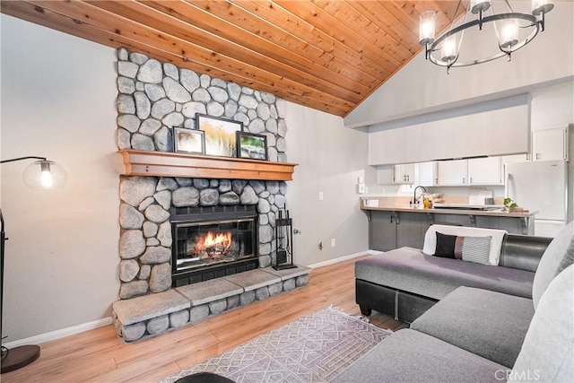 living room featuring wooden ceiling, a stone fireplace, sink, a notable chandelier, and light hardwood / wood-style floors