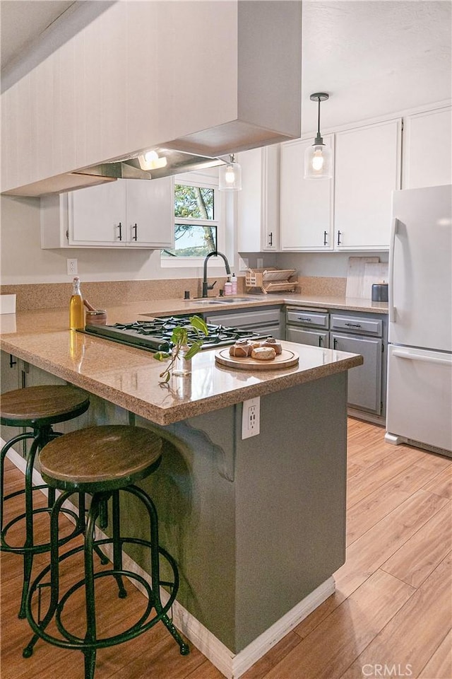 kitchen with white cabinetry, hanging light fixtures, kitchen peninsula, white fridge, and light wood-type flooring