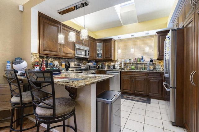 kitchen with decorative backsplash, appliances with stainless steel finishes, dark stone counters, sink, and a breakfast bar area