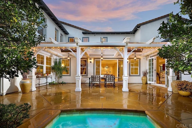 back house at dusk featuring a pergola and a patio