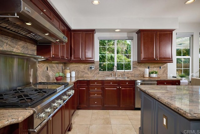 kitchen with light stone counters, stainless steel appliances, a sink, dark brown cabinets, and extractor fan