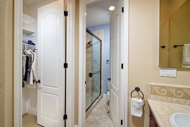 full bathroom featuring tile patterned flooring, toilet, vanity, a spacious closet, and a stall shower