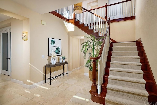 stairway featuring tile patterned flooring, a towering ceiling, and baseboards