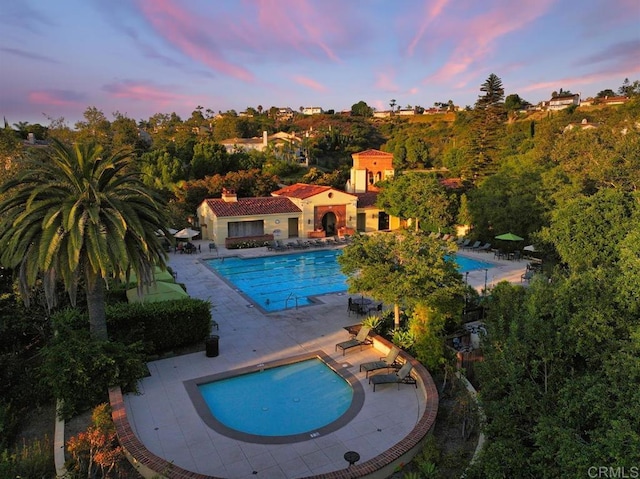 pool at dusk featuring a community pool and a patio