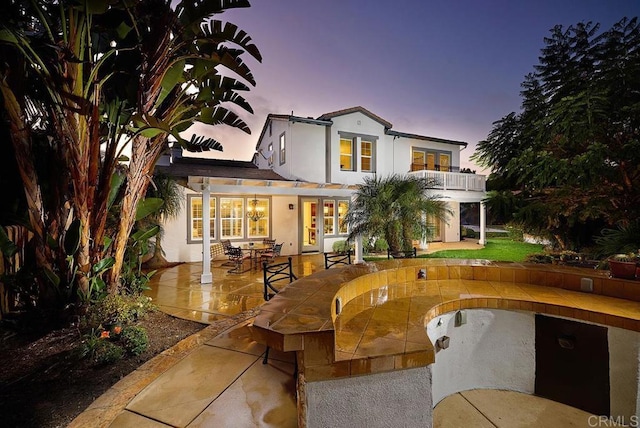 rear view of house with a patio, a balcony, and stucco siding