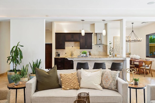 kitchen with pendant lighting, tasteful backsplash, a notable chandelier, dark brown cabinetry, and a kitchen bar