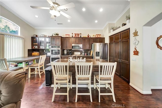 kitchen featuring ornamental molding, stainless steel appliances, a center island, dark hardwood / wood-style floors, and a breakfast bar area