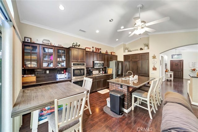 kitchen with dark brown cabinetry, sink, stainless steel appliances, crown molding, and an island with sink