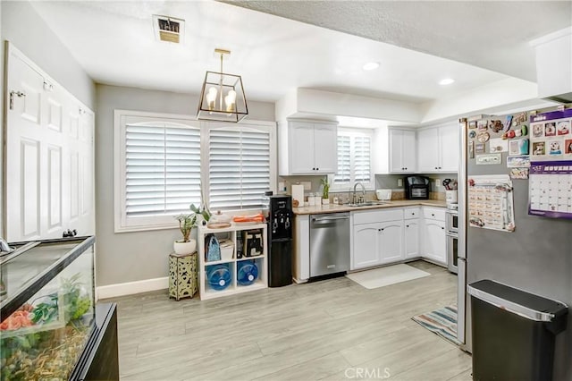 kitchen featuring sink, hanging light fixtures, light hardwood / wood-style flooring, white cabinetry, and stainless steel appliances