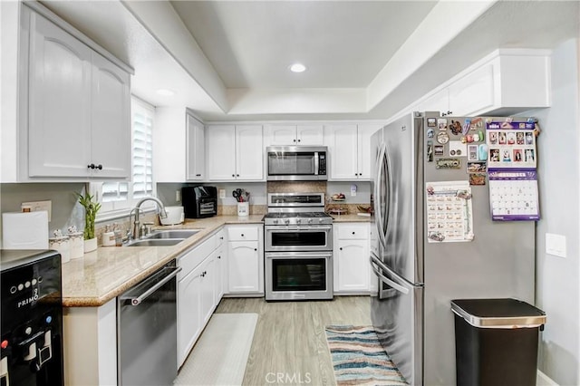 kitchen with white cabinetry, sink, light hardwood / wood-style flooring, a tray ceiling, and appliances with stainless steel finishes