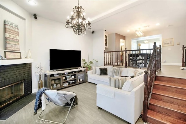 living room with wood-type flooring, a chandelier, and a brick fireplace