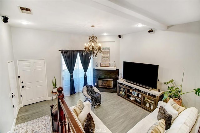 living room with hardwood / wood-style flooring, beam ceiling, a fireplace, and an inviting chandelier