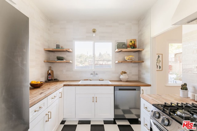 kitchen featuring wooden counters, appliances with stainless steel finishes, a wealth of natural light, sink, and white cabinets