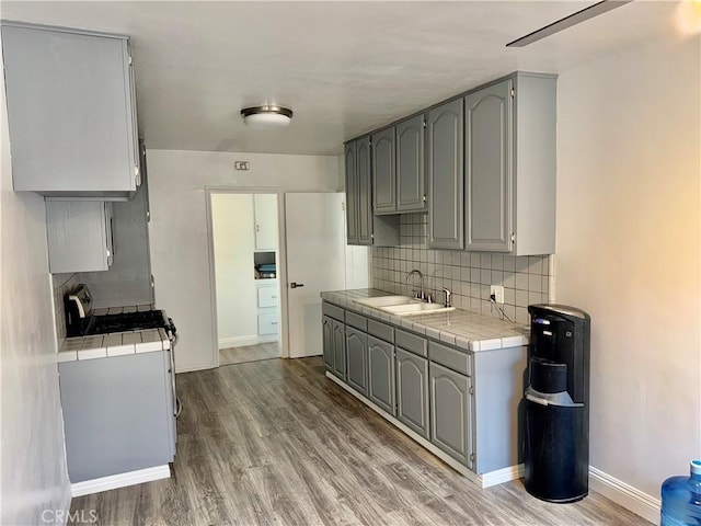 kitchen featuring sink, light hardwood / wood-style flooring, tile countertops, gray cabinets, and decorative backsplash