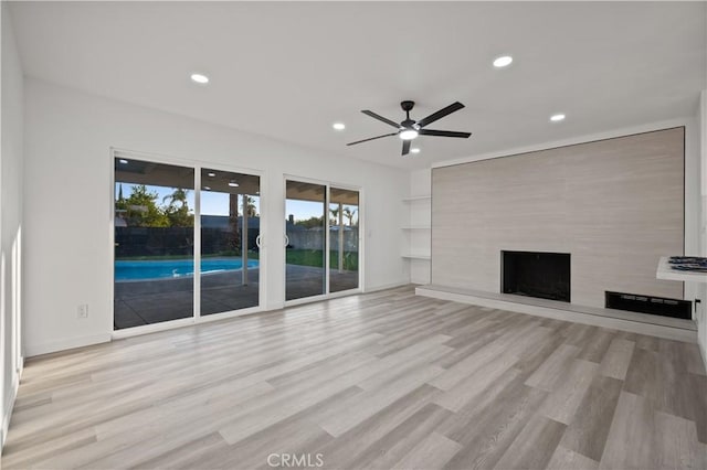 unfurnished living room with ceiling fan, a large fireplace, and light hardwood / wood-style flooring