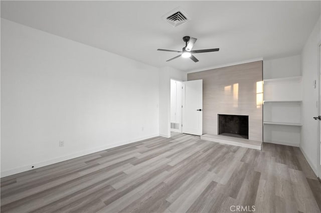 unfurnished living room with light wood-type flooring, a large fireplace, and ceiling fan