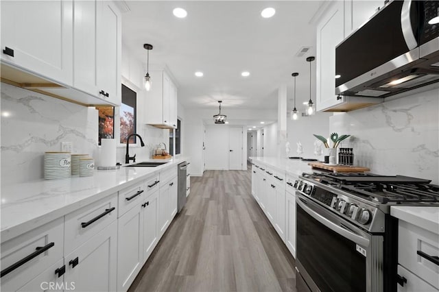 kitchen featuring tasteful backsplash, white cabinets, stainless steel appliances, and decorative light fixtures