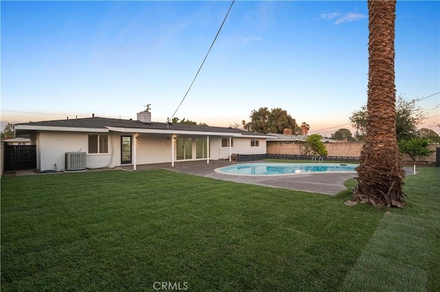 back house at dusk featuring a lawn, a fenced in pool, and central air condition unit