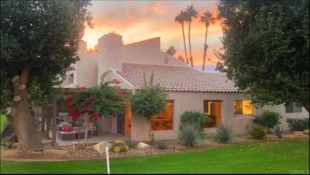 back house at dusk with a lawn and a patio