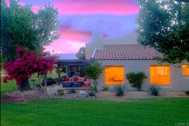 back house at dusk with an outdoor living space, a pergola, a patio area, and a lawn