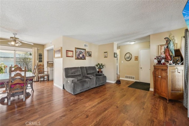 living room with a textured ceiling, ceiling fan, and dark wood-type flooring