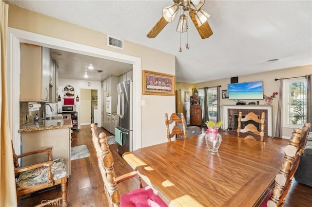 dining space featuring plenty of natural light, ceiling fan, a fireplace, and dark wood-type flooring