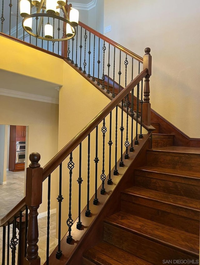 stairs featuring ornamental molding, a towering ceiling, and a notable chandelier