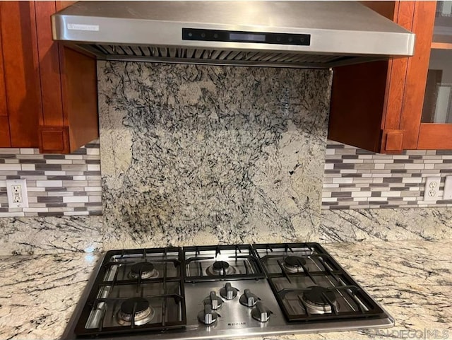 interior space featuring tasteful backsplash, light stone counters, wall chimney exhaust hood, and stainless steel gas cooktop