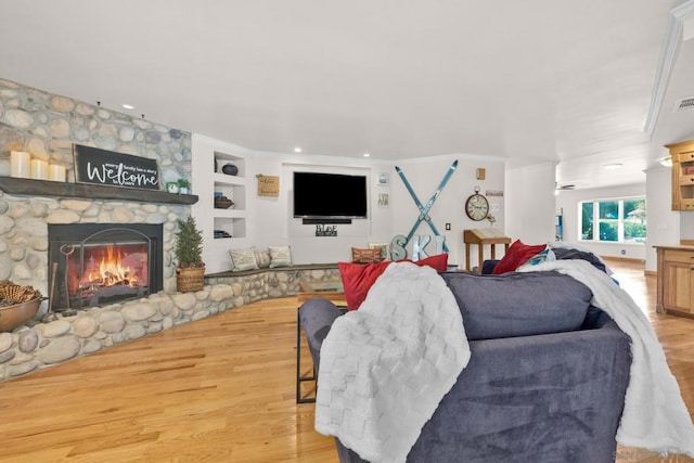 living room featuring built in shelves, light hardwood / wood-style flooring, crown molding, and a stone fireplace