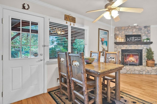 dining area with ceiling fan, crown molding, wood-type flooring, and a stone fireplace