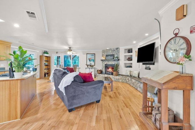 living room featuring ceiling fan, a fireplace, light hardwood / wood-style flooring, built in features, and ornamental molding