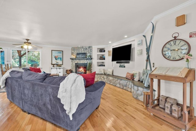 living room with ceiling fan, built in shelves, a stone fireplace, and ornamental molding