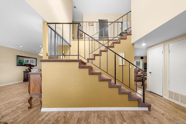 stairs with baseboards, a high ceiling, visible vents, and wood finished floors