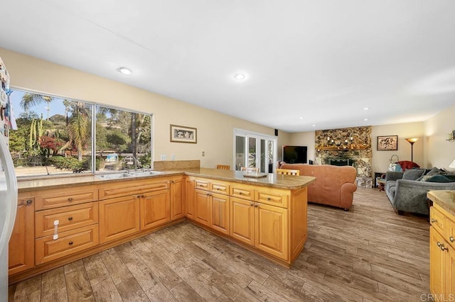 kitchen featuring light wood finished floors, open floor plan, a peninsula, a fireplace, and a sink