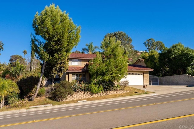 view of property hidden behind natural elements featuring a garage, a tile roof, concrete driveway, and stucco siding