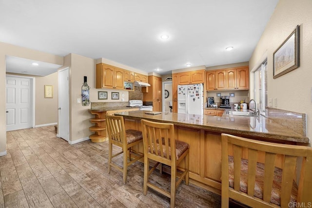 kitchen featuring white appliances, light wood finished floors, a peninsula, a kitchen bar, and a sink