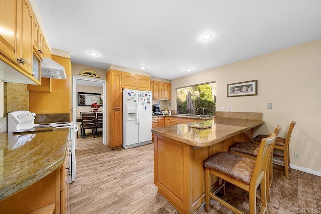 kitchen featuring a peninsula, white appliances, light wood-style floors, ventilation hood, and a kitchen bar