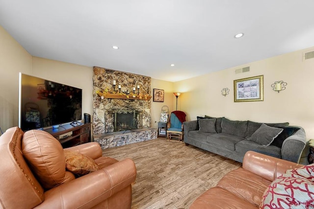 living room featuring a stone fireplace, light wood-type flooring, visible vents, and recessed lighting