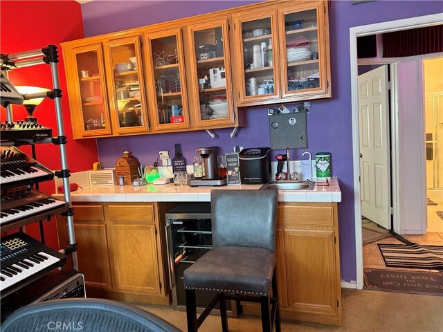 bar featuring tile counters, light carpet, sink, and beverage cooler