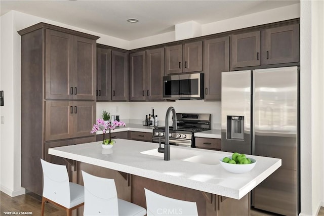 kitchen featuring dark hardwood / wood-style floors, an island with sink, appliances with stainless steel finishes, dark brown cabinets, and a kitchen bar