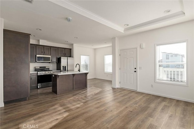 kitchen with a center island with sink, a raised ceiling, dark hardwood / wood-style floors, appliances with stainless steel finishes, and dark brown cabinetry