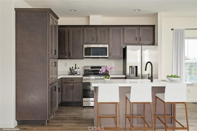 kitchen with a kitchen island with sink, sink, dark hardwood / wood-style floors, appliances with stainless steel finishes, and dark brown cabinetry