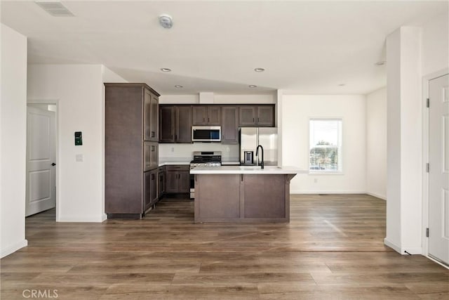 kitchen featuring dark brown cabinets, dark hardwood / wood-style flooring, an island with sink, and appliances with stainless steel finishes